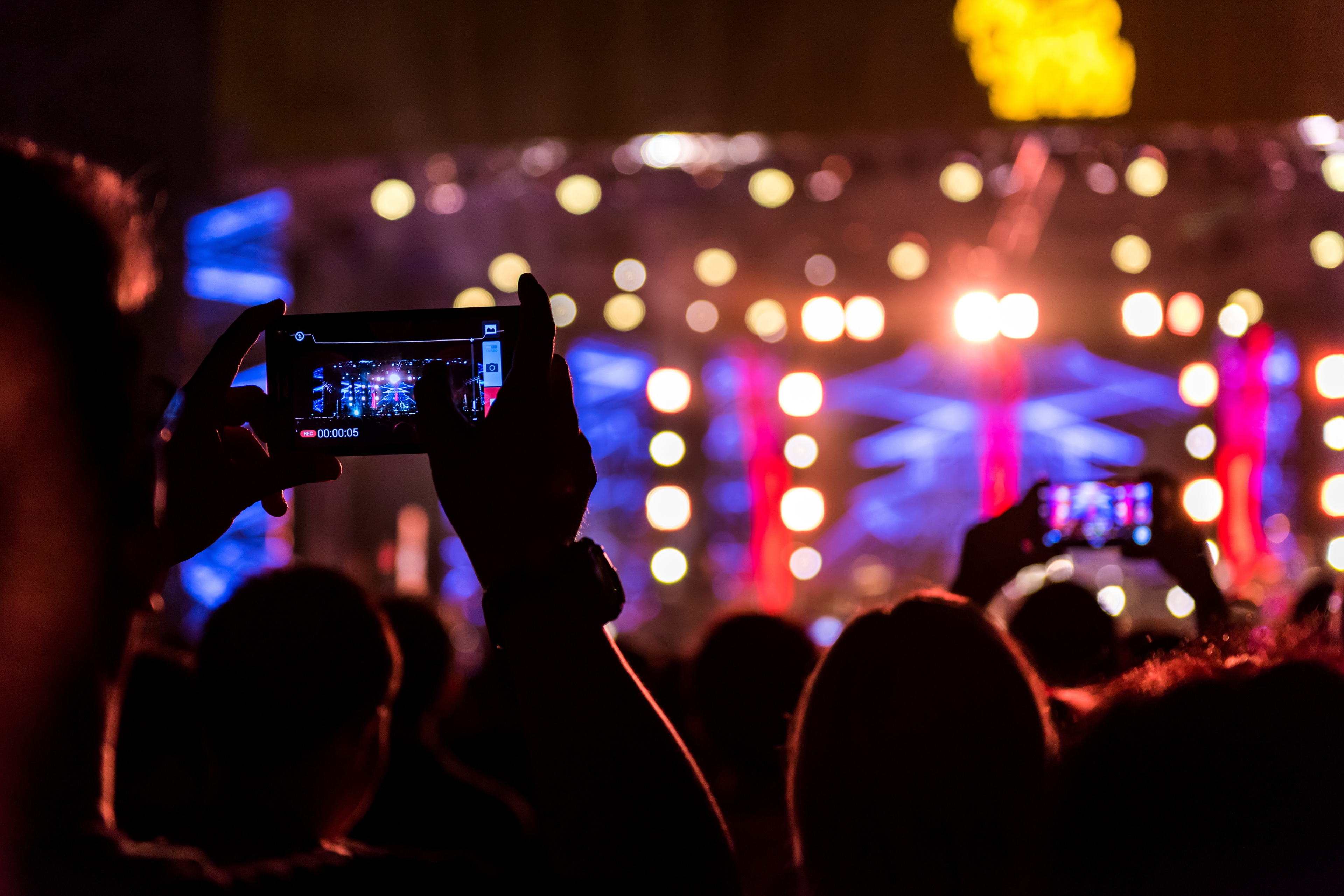 Man in a suit smiling and enjoying an event under bright stage lights.